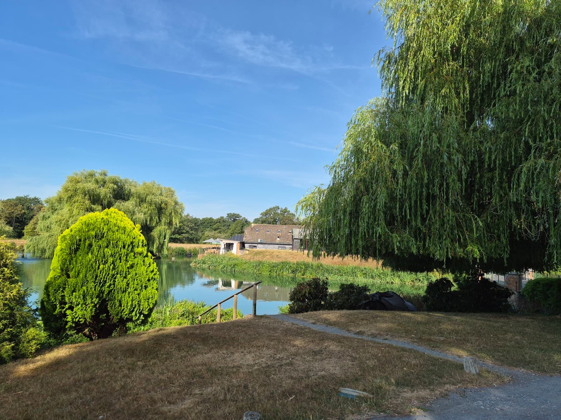 The lake with the fish farm buildings on the far bank, under a clear morning sky