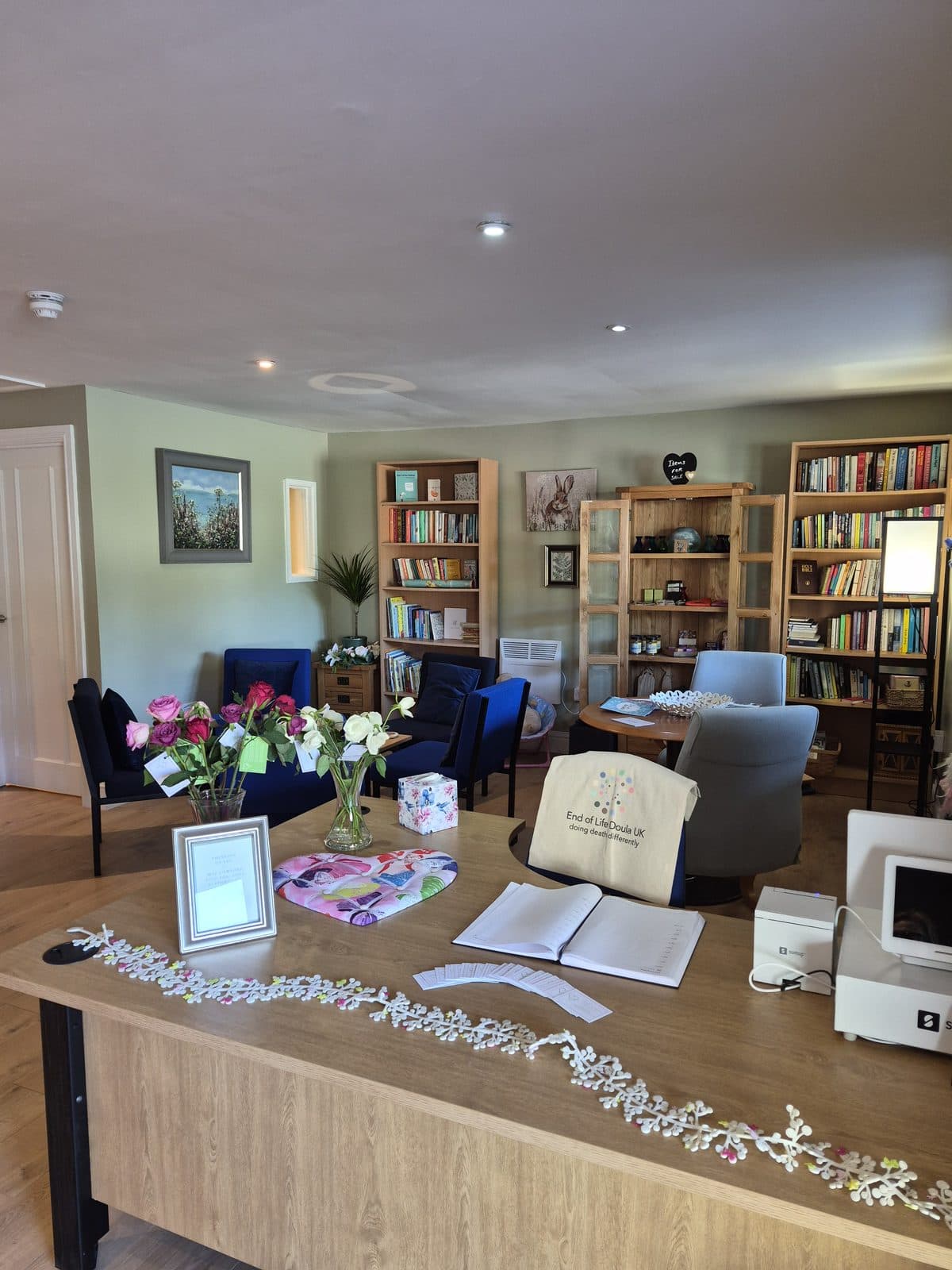 The welcome room, with armchairs, bookshelves, a vase of roses and a visitors' book on the desk